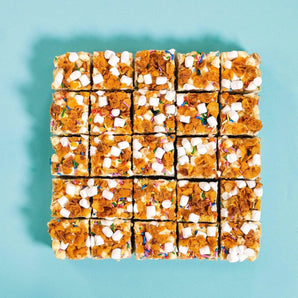 Cereal Milk Rocky Road squares topped with crunchy cornflakes, malted marshmallows, and rainbow sprinkles by Crumbs & Doilies